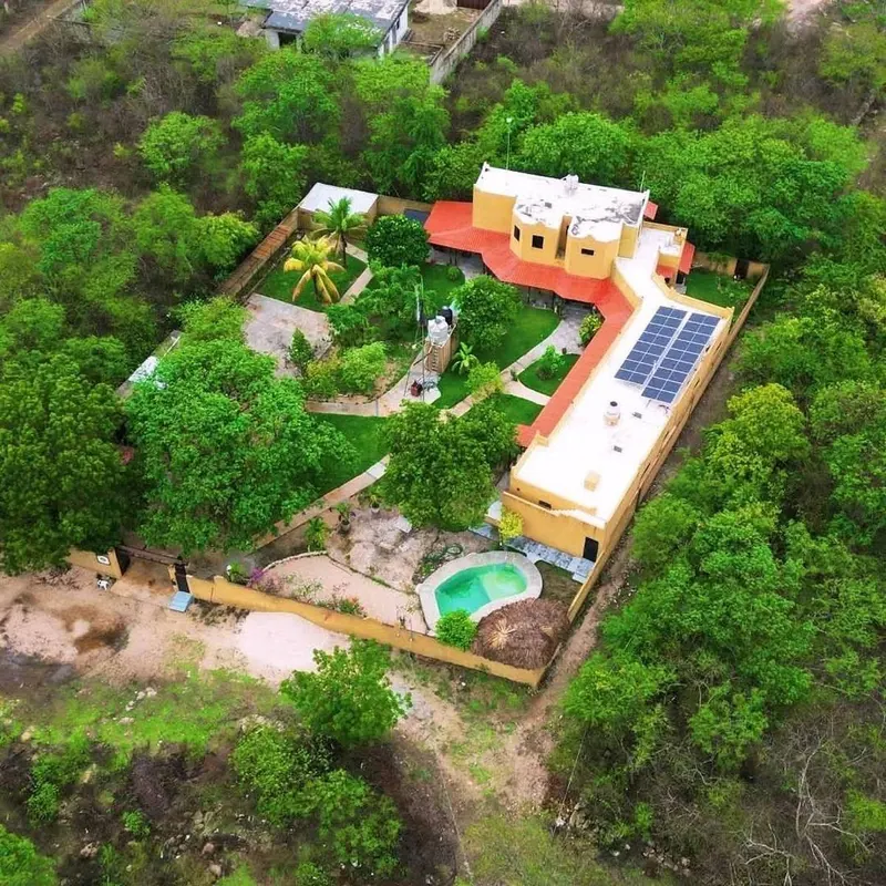 Vista aérea de toda la propiedad bardeada: casa, patio, paneles solares, alberca y palapa.