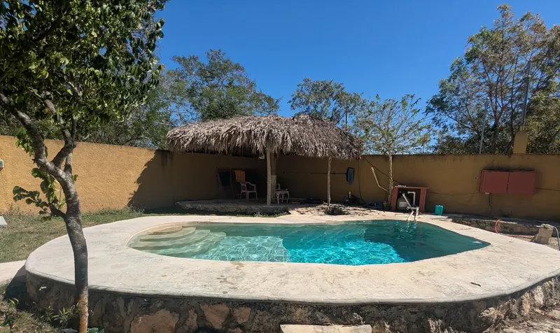 La alberca con borde de piedra caliza y la palapa, bajo un cielo azul.